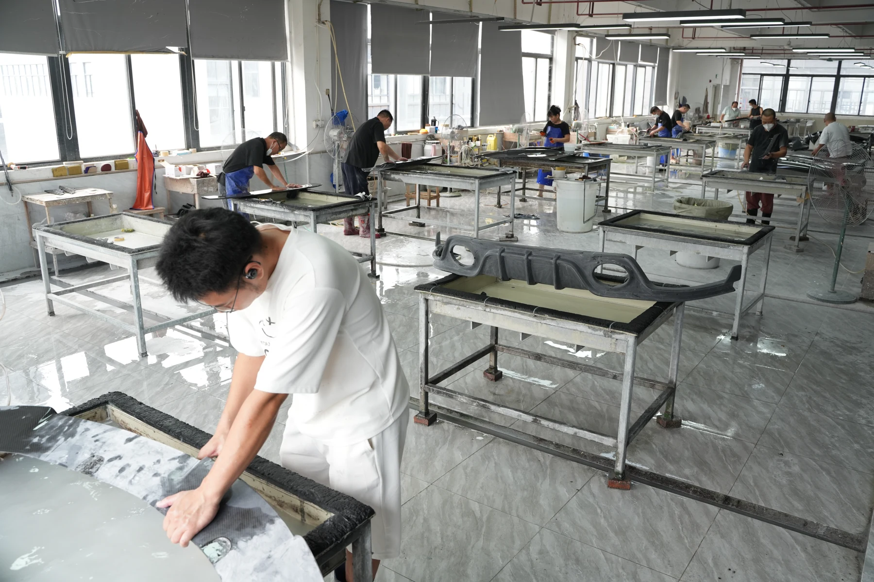 A technician wet-sanding a carbon fiber diffuser by hand on the finishing floor